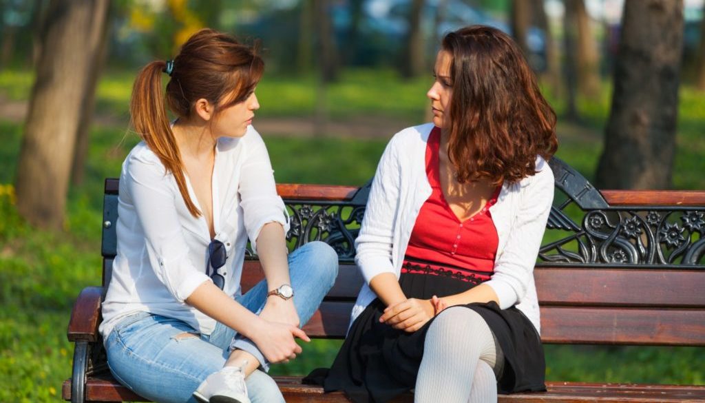 Two,Best,Friends,Talking,Outside,,Sitting,On,A,Bench,In